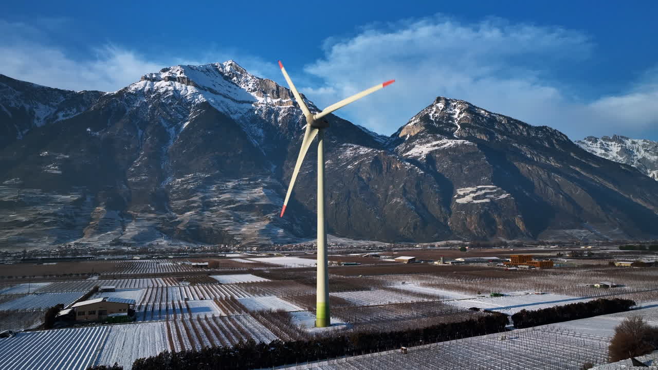 커다란 현대식 풍차가 거대한 알프스를 배경으로 화창한 겨울날 론 계곡에서 회전합니다.