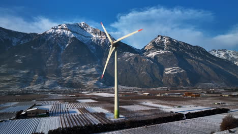 un gran molino de viento moderno gira en el valle del ródano en un soleado día de invierno con los alpes gigantes en el fondo