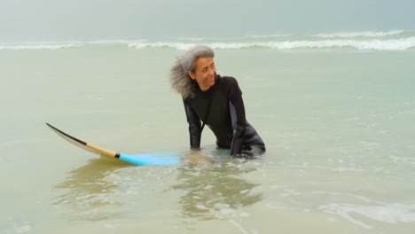 front view of active senior african american female surfer sitting on surfboard in the sea 4k