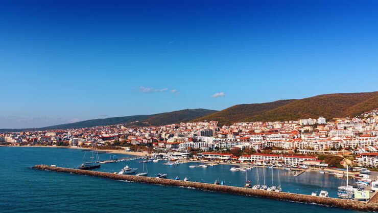 Volo sul paesaggio acquatico blu lungo la diga e i moli con le barche. Prospettiva aerea sulla zona turistica della Bulgaria in una giornata di sole.