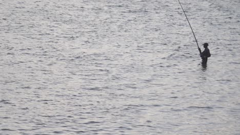 Fisherman-standing-hip-high-deep-in-the-sea-holding-fishing-rod-action-silhouette-scenic-evening-time-slow-motion-b-roll-clip,-Galle-Dutch-Fort,-Sri-Lanka,-hand-held-panning-shot