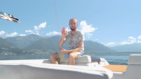slow-motion man sitting back boat waving at camera, on a beautiful sunny clear sky in italy