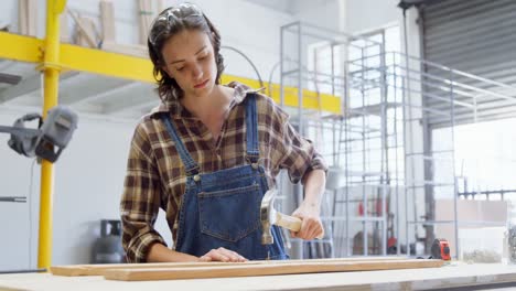 female welder hammering nail on a wooden plank 4k