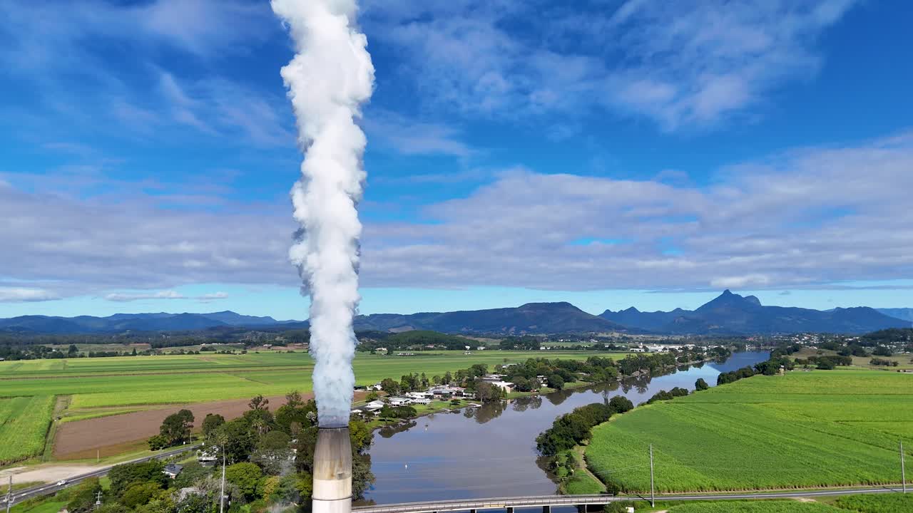 Drone footage captures sugarcane fields, a factory emitting steam, and a winding river under a bright blue sky