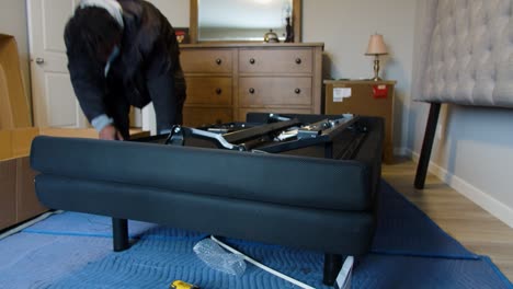 two delivery movers maneuvering mattress power base into place under upholstered headboard in customer’s room