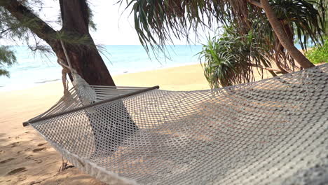 a knotted white hammock hangs between trees over a sandy beach