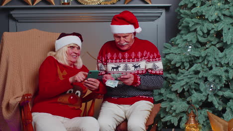 Senior-family-couple-searching-purchase-online-Christmas-gifts-in-mobile-phone-application-at-home