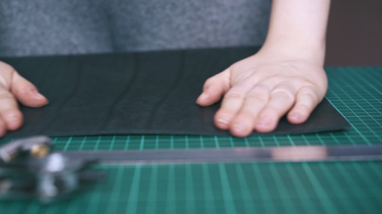 숙련 된 맞춤사 는 초록색 매트 보드 에 검은색 가죽 천 을 놓는다