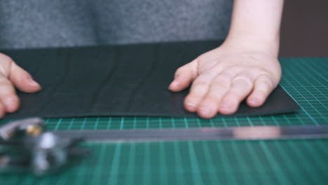 skilled tailor puts black leather fabric on green mat board