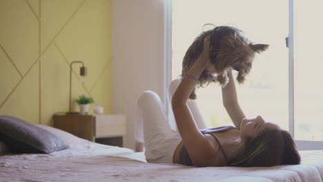 Woman-Lifting-Her-Dog-In-The-Air-And-Lying-On-Bed