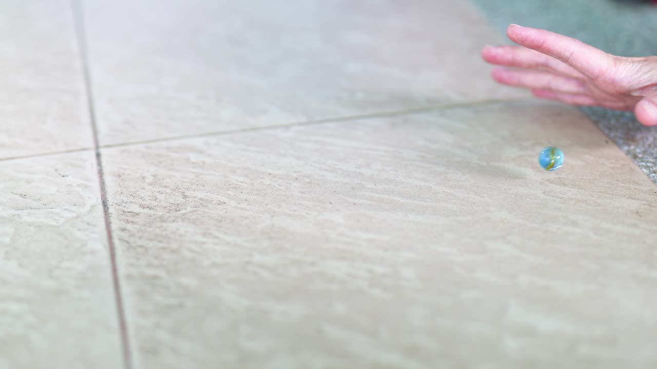 una mano suelta las canicas sobre un piso de azulejos, capturando su movimiento y dispersión. la iluminación brillante y natural realza la escena