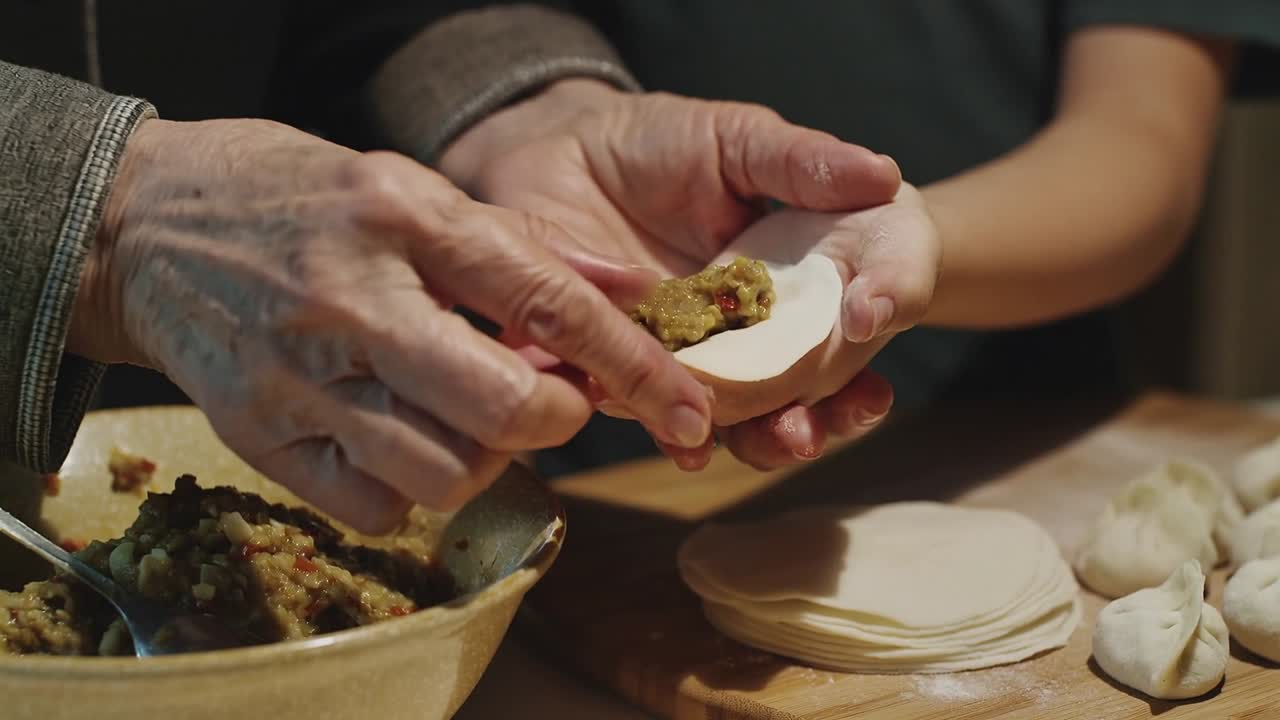 Scooping veg filling starting senior guiding child in pleating dumpling in kitchen for family meal