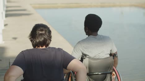 Rear-view-of-male-and-female-friends-using-wheelchairs-walking