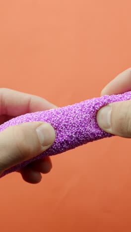 hands stretching pink bead slime on orange background in close-up, vertical
