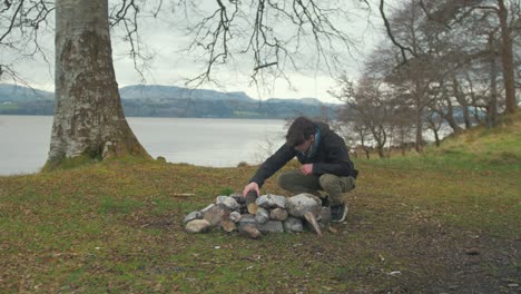 wideshot young man preparing campfire on island in winter