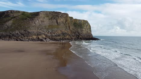 aerial drone shot on mewslade bay in gower peninsula with dramatic coastal cliff and rolling sea waves and blue sky 4k