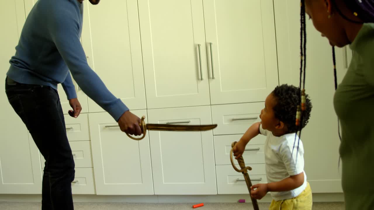 편안한 집에서 장난감 검을 가지고 놀고 있는 젊은 흑인 아버지와 아들의 측면 전망 4k