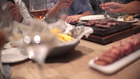 friends eating at restaurant celebrating birthday in dinning room, toasts, cheers and preparing their own meat at hot stone