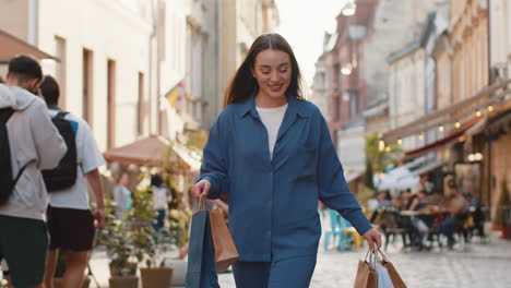 happy young woman shopaholic consumer after shopping sale with full bags walking in city street