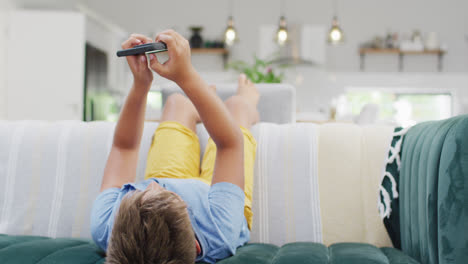 Happy-caucasian-boy-lying-on-sofa-and-using-smartphone,-slow-motion