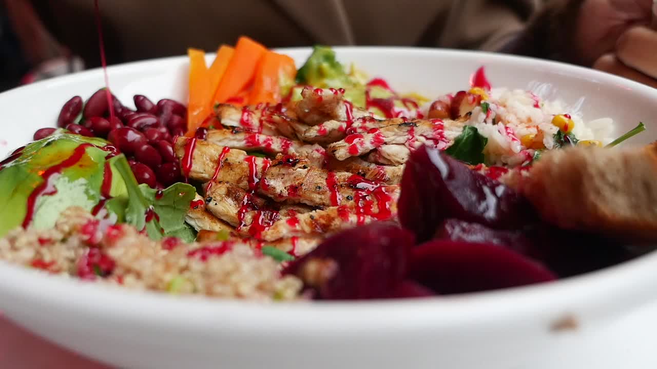 Nærbilde av rød saus som dryppes over en sunn kyllingsalatbolle