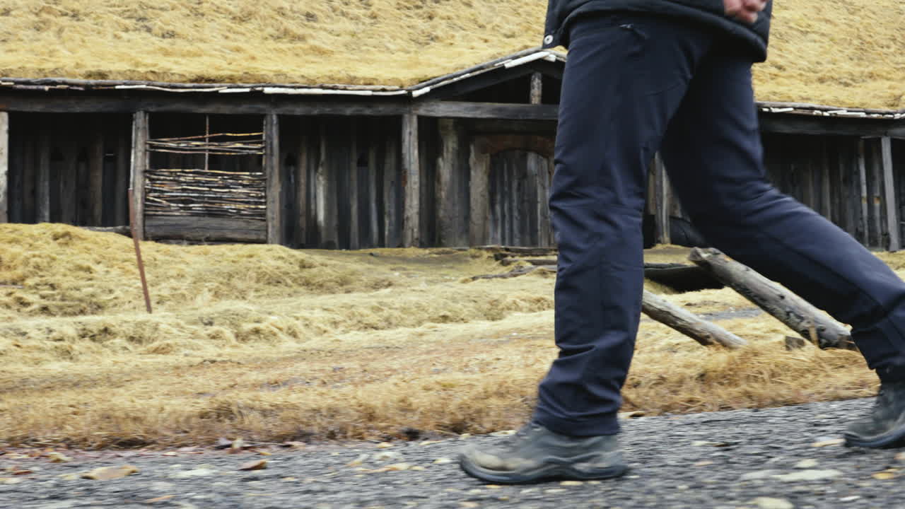 나무 잔디집, 바이킹 스타일의 건물, 가까운 길을  ⁇ 는 사람의 진 ⁇  부츠와 다리