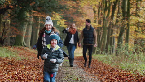 smiling family walking with dog along path through autumn countryside with children running ahead