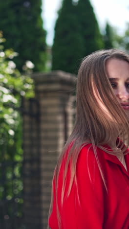passionate young girl posing to camera. beautiful young model in red dress with long hair on the green trees background. sexy woman turning around herself joyfully. vertical video