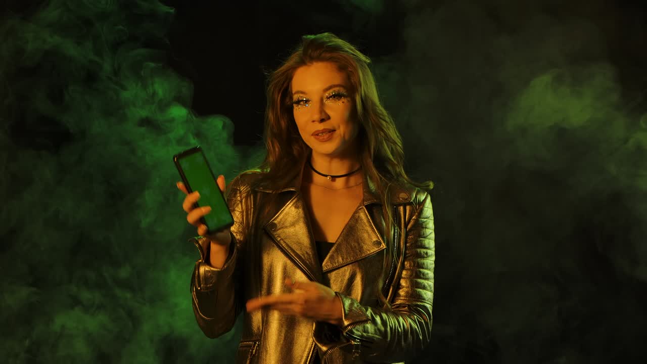 retrato de una mujer joven y bonita está enviando mensajes de texto en su teléfono, luego muestra un teléfono inteligente con una tecla de croma de pantalla verde y mostrando el pulgar hacia arriba con un gesto.