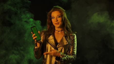 retrato de una mujer joven y bonita está enviando mensajes de texto en su teléfono, luego muestra un teléfono inteligente con una tecla de croma de pantalla verde y mostrando el pulgar hacia arriba con un gesto.