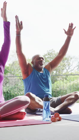 vertical video of happy diverse senior couple practicing yoga meditation sitting outdoors