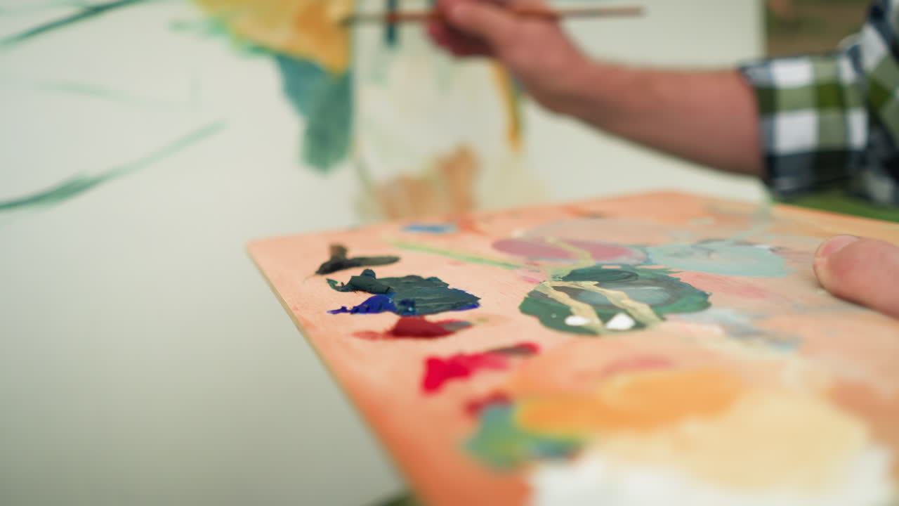 A painter holds a wooden palette full of vibrant paint colors while adding the final touches to a canvas. focusing on the palette filled with mixed paints and the delicate motion of the brush