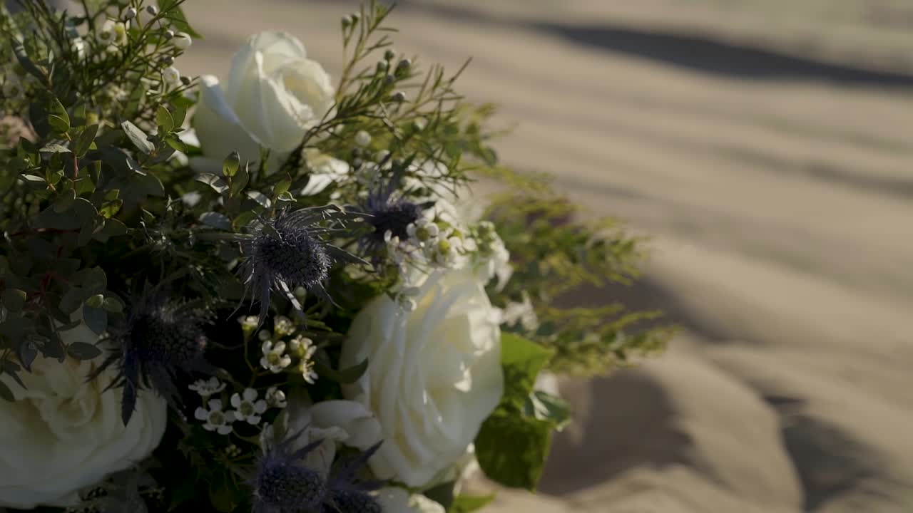 Close up of a white rose with thistle wedding bouquet blowing in the wind placed on the sand of the Little Sahara sand dunes in Joab, UT