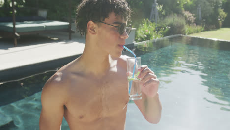 happy biracial man drinking drink at pool in garden on sunny day