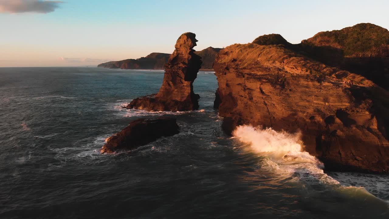altas olas lavan los acantilados de la playa de piha que están pintados en colores cálidos en la hora dorada