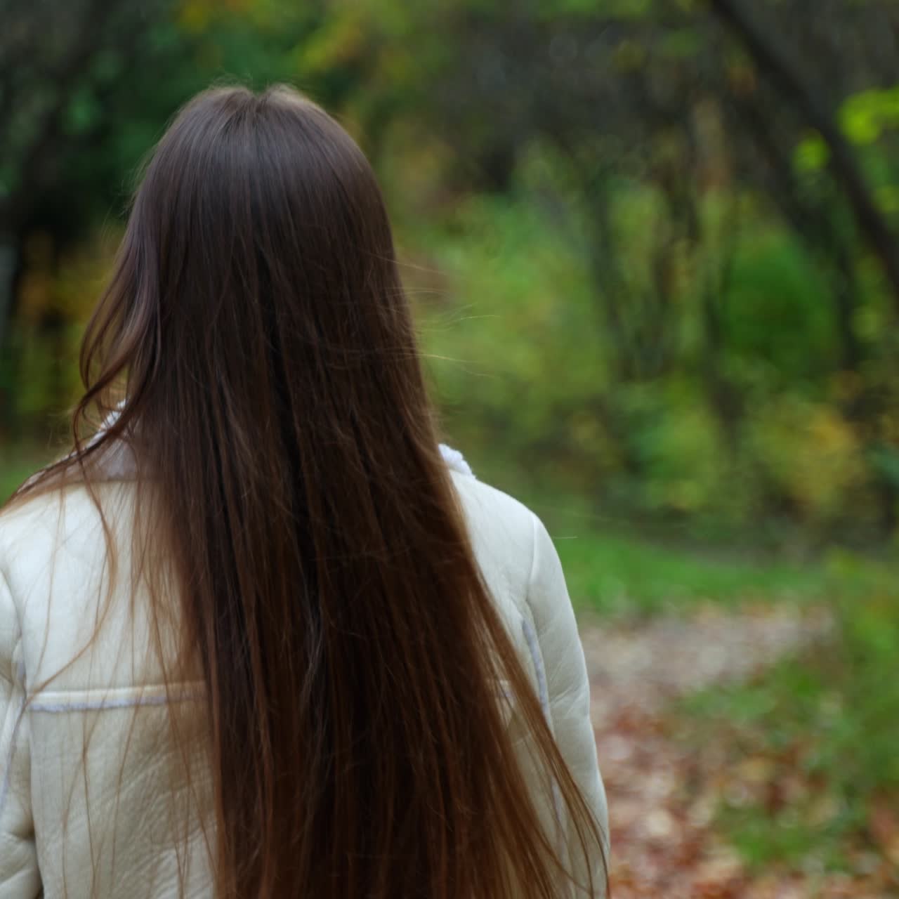 Cheerful lady holding a paper cup walks by the park looking back into camera. Smiling woman making inviting gesture with her hand calling to follow her