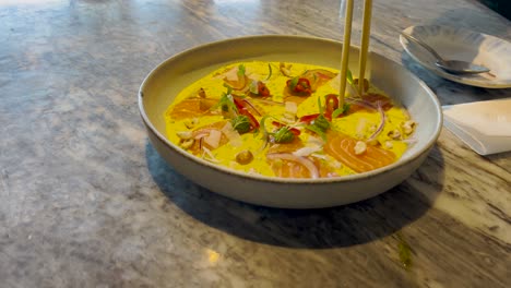 bowl of vibrant soup with vegetables and raw fish on marble table indoors in bright ambient restaurant light