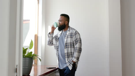 african american man drinking coffee and looking out window at home, slow motion