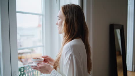 mujer satisfecha disfrutando de una taza de café en casa de cerca. mujer mirando por la ventana