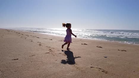 toddler girl running on the beach towards the ocean