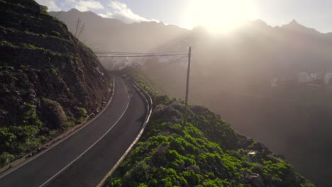 Vista-Aérea-De-Los-Coches-Que-Conducen-A-Lo-Largo-De-La-Carretera-De-Montaña-Boscosa-Verde-En-Anaga,-Tenerife-Con-Luz-Solar-Cálida-Y-Escénica-En-El-Horizonte