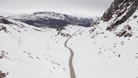 carretera abandonada entre altas montañas cubiertas de nieve blanca en un día nublado en noruega