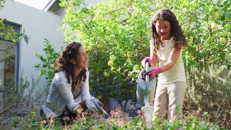 Mixed-race-mother-and-daughter-gardening-in-sunny-garden,-watering-plants