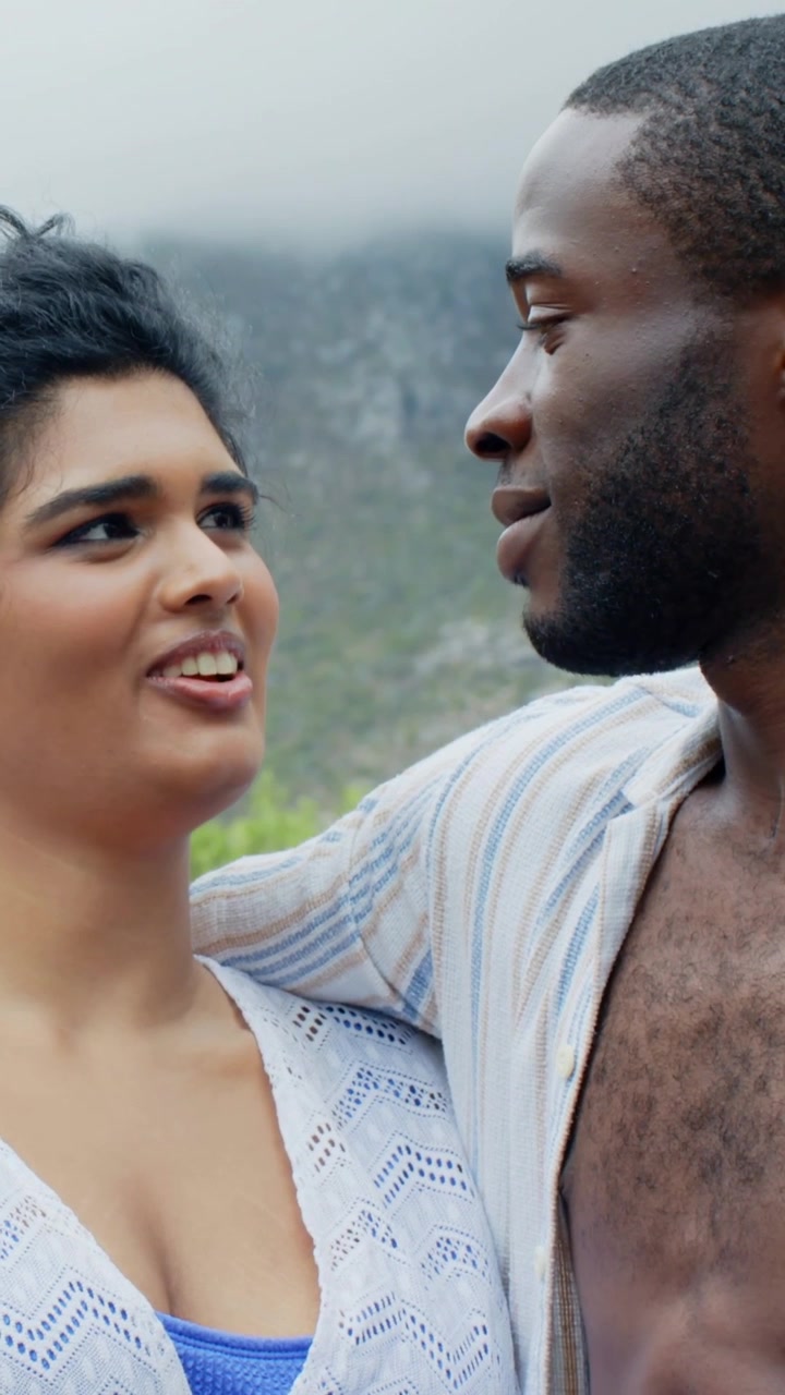Vídeo vertical: Casal apaixonado sorrindo em encosta nebulosa, homem falando, mulher respondendo, blusa azul