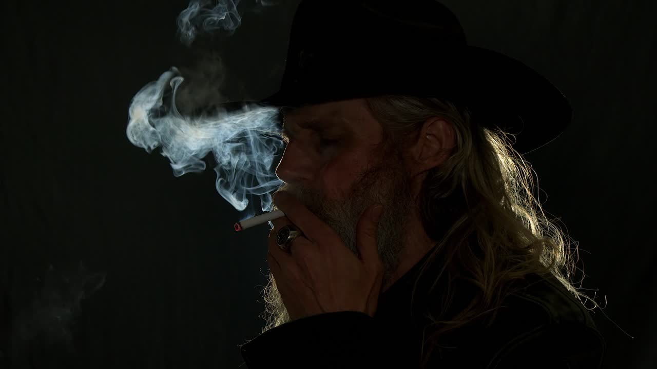 Bearded cowboy with rim lighting lights smoke, dark and moody close-up