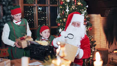 elves bring gift boxes to santa claus, who sits at a table in a room with christmas decorations and a christmas tree. santa is reading text through a magnifying glass