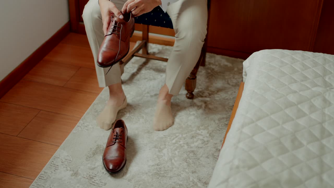 Groom sitting on a chair, putting on polished brown leather dress shoes before the ceremony