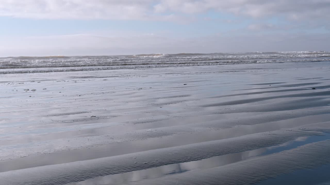 Waves gently roll across a serene coastal beach under soft light and scattered clouds