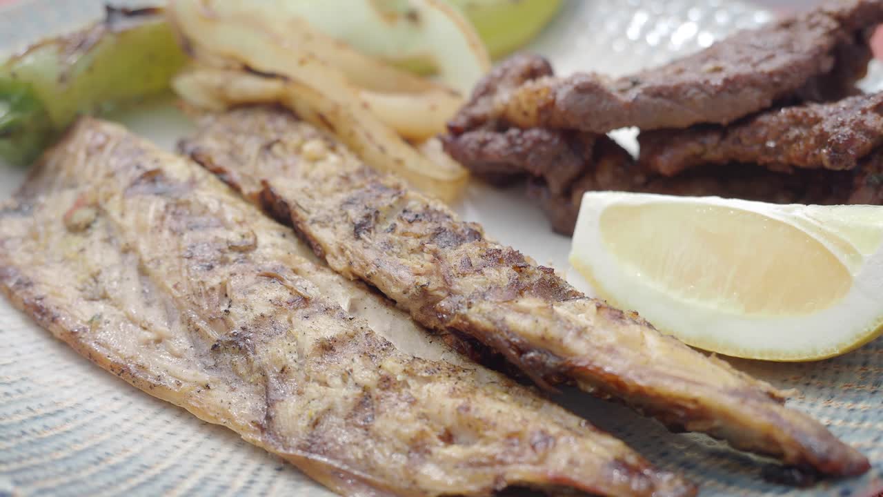 Pesce e carne alla griglia con verdure e limone serviti su un piatto