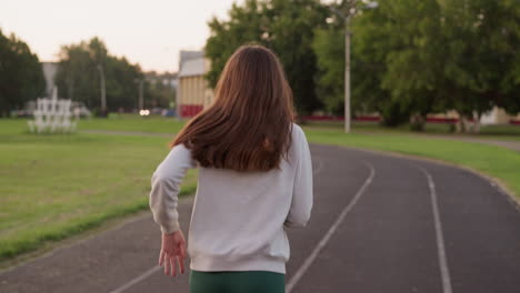 woman jogging along sport stadium track. active pastime and improving endurance at sunset. cardio workout alone for good blood circulation of lady